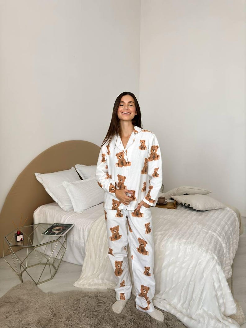 以下が含まれることがあります： 茶色のテディベアの繰り返し模様が特徴の白いパジャマセット。セットには、ボタンダウンシャツとマッチングパンツが含まれています。パジャマは柔らかい生地でできており、寝間着やラウンジウェアに適しています。
