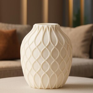 Può includere: Vaso decorativo color crema con un motivo geometrico strutturato. Il vaso ha una base ampia e un collo più stretto. La superficie è ricoperta da un motivo ripetitivo e interconnesso. Il vaso è appoggiato su un tavolo colorato chiaro.