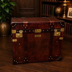 May include: A vintage-style, rectangular trunk with a rich, dark brown leather exterior. The trunk features brass hardware, including corner protectors, latches, and decorative accents. The trunk is a classic piece of luggage or storage.
