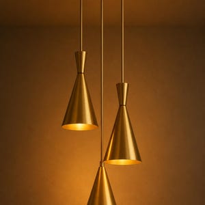 Puede incluir: Una moderna lámpara colgante con tres pantallas en forma de cono de color dorado. Las pantallas cuelgan de un soporte circular en el techo, creando una solución de iluminación elegante y contemporánea. El interior de las pantallas emite una luz cálida.