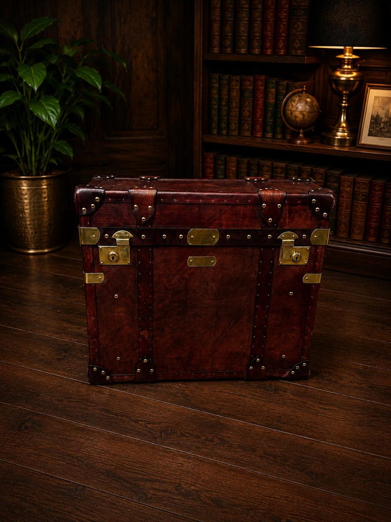 May include: A vintage-style, rectangular trunk made of dark brown leather with brass hardware. The trunk features metal studs, corner protectors, and brass locks. It is a classic piece of luggage or storage.