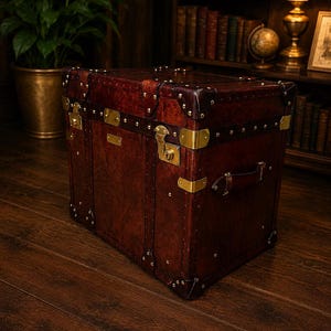 May include: A vintage-style, dark brown leather trunk with brass hardware, including corner protectors, clasps, and rivets. The trunk features a handle and is set on a wooden floor, suggesting a travel or storage theme.