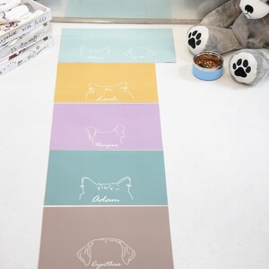 May include: A collection of colorful pet placemats. Each placemat features a pet's name and a line drawing of a cat or dog. The placemats are in shades of blue, yellow, purple, and brown.