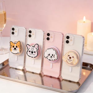 Può includere: Quattro custodie trasparenti per telefono con disegni di cani dei cartoni animati su un vassoio d'argento. Le custodie presentano diverse razze di cani nei colori arancione, nero, bianco e beige. Lo sfondo comprende candele e un bicchiere di champagne.