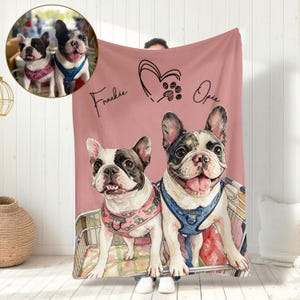 May include: A pink blanket with a watercolour illustration of two French Bulldogs. The blanket is personalised with the names "Frankie" and "Opie", a heart and paw print design. The dogs are wearing harnesses.