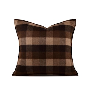 May include: A square decorative pillow with a brown and tan plaid pattern. The pillow has a soft, textured appearance and a classic design. The color palette includes shades of brown and beige, creating a warm and inviting aesthetic.