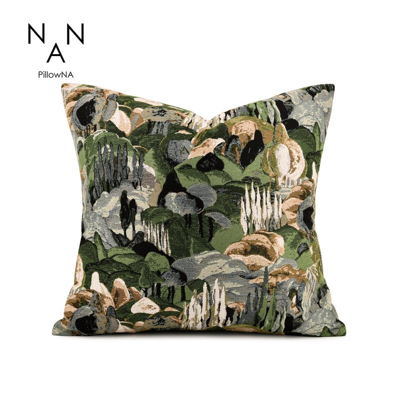 May include: A square throw pillow featuring a woven tapestry design of a landscape with rolling hills, trees, and rock formations in shades of forest green, olive, beige, black, and grey. The text NAN A PillowNA is printed in the upper left corner.