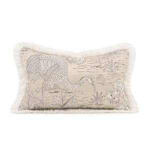 May include: Rectangular decorative pillow with a beige background featuring a crane illustration in gray tones. The pillow has a white fringe border. The crane is depicted in a marshy environment with plants and flowers.