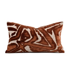 May include: A rectangular throw pillow featuring a plush, velvet-like texture in a deep rust-brown color. The surface displays a large-scale, abstract pattern of interconnected shapes in a contrasting light beige, with a small white tag labeled echo.