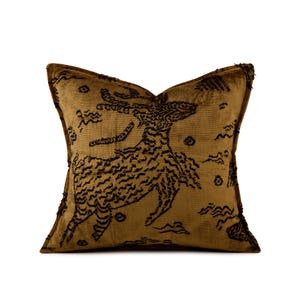 May include: A square throw pillow in a deep mustard gold color featuring a dark brown embroidered design of a leaping deer. The embroidery has a textured, raised appearance with additional small abstract shapes scattered across the fabric surface.