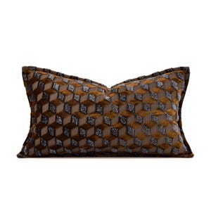 May include: A rectangular throw pillow featuring a repeating geometric cube pattern in shades of brown and metallic silver. The fabric has a textured, velvet-like appearance with a piped edge border, creating a three-dimensional visual effect.