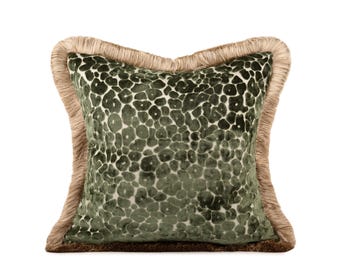 May include: A square throw pillow featuring a dark olive green velvet fabric with a textured leopard spot pattern. The edges of the pillow are finished with a thick, light tan fringe trim that extends along all four sides of the square cushion.