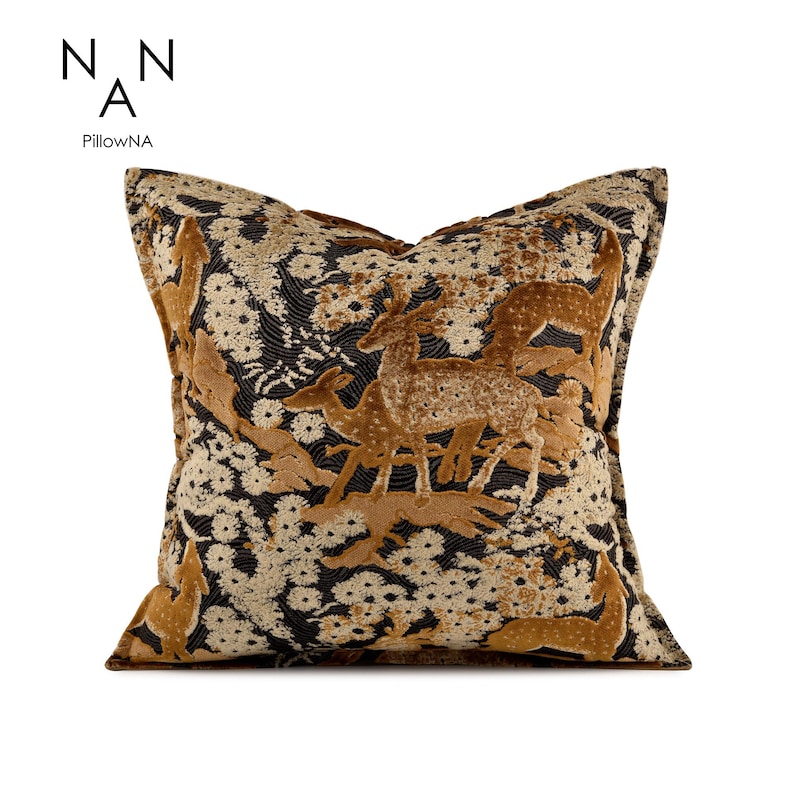 May include: Square cushion with a deer and floral design. The cushion features a brown and gold deer scene against a black and cream floral background. The brand name "PillowNA" is printed in the upper left corner.