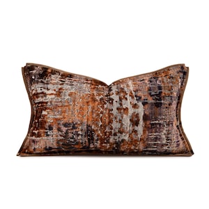 May include: A rectangular throw pillow featuring a textured, multi-tonal fabric with a blend of deep brown, burnt orange, and metallic silver hues. The pillow has a distinct piped edge border and a structured, slightly flared shape at the corners.