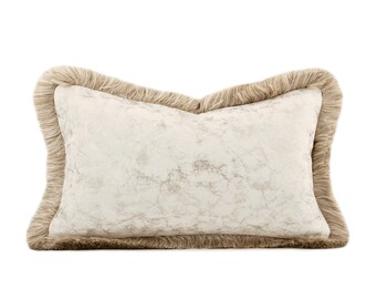 May include: Rectangular decorative pillow with a cream-colored marble-like pattern. The pillow has a fringed border in a light brown color. The pillow is designed for home decor and adds a touch of elegance to any space.