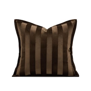 May include: A square decorative pillow with a brown striped pattern. The pillow has a soft, velvety texture and a neutral color palette, suitable for various interior design styles. The pillow is a home decor item.