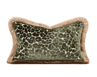 May include: A rectangular throw pillow featuring a dark olive green velvet fabric with a raised leopard print pattern. The pillow is bordered by a thick, textured tan fringe trim that extends along all four edges, creating a soft, layered appearance.