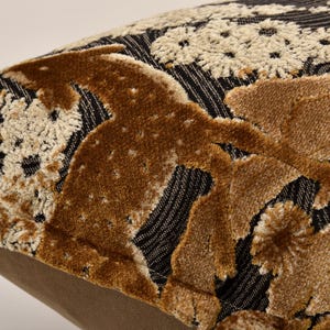 May include: Close-up of a decorative cushion with a textured design. The cushion has a black background with vertical white stripes and a raised, patterned design in shades of brown and beige. The cushion's edge is a solid tan colour.