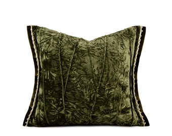 May include: A square olive green velvet throw pillow with a crushed texture and diagonal stitched lines across the front. The edges are finished with a dark green border and a delicate white beaded trim along the vertical sides of the pillow.