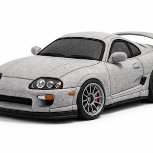May include: A grey toy car with a spoiler, side mirrors, and detailed wheels. The car has a black front bumper and a dark windscreen. The car is made of a soft material and resembles a sports car.