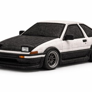 Puede incluir: Un coche deportivo blanco y negro con faros emergentes. El coche tiene un capó negro, molduras negras y ruedas negras. El coche es un coupé con alerón trasero, sobre un fondo blanco.