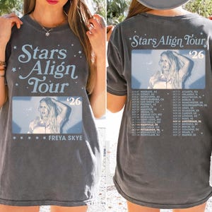 Puede incluir: Camiseta gris oscuro con "Stars Align Tour '26" y una foto de Freya Skye. El frente y la espalda muestran las fechas de la gira. La camiseta tiene un estilo vintage.