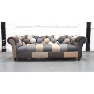 May include: A button-backed sofa with a patchwork design in various neutral tones. The sofa features a mix of grey, beige, and brown panels. It has rolled arms and wooden legs, offering a classic and stylish seating option for a living room or lounge area.