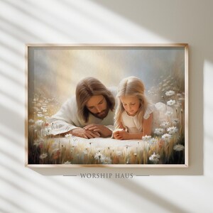 Op de afbeelding: Ingelijste print met een serene scène van twee figuren in een veld met witte bloemen. Eén figuur draagt een wit gewaad, de andere is een jong meisje in een witte jurk. De tekst "WORSHIP HAUS" staat onderaan.