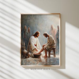 Puede incluir: Obra de arte enmarcada que representa una escena bíblica del lavatorio de pies. La pintura presenta figuras con túnicas, con tonos cálidos y terrosos. El texto "WORSHIP HAUS" está impreso en la parte inferior del marco.