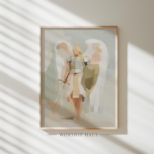 May include: Framed art print featuring a stylized depiction of an angel with a sword. The artwork uses a muted color palette of beige, white, and light green. The text "WORSHIP HAUS" is printed at the bottom of the frame.