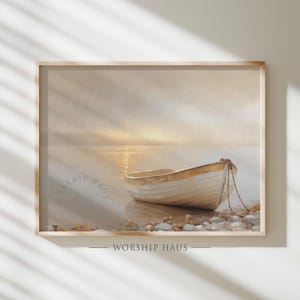 May include: A framed watercolor print depicts a small, off-white boat on a shoreline at sunset. The boat is tied to the shore with a rope. The water reflects the golden light of the setting sun. The words "WORSHIP HAUS" are printed on the bottom of the frame.