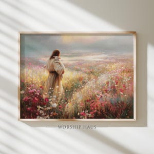 Op de afbeelding: Een ingelijste print toont een figuur in een gewaad die een lam draagt in een veld met wilde bloemen. Het kunstwerk heeft een zachte, schilderachtige stijl met warme, natuurlijke tinten. De tekst "WORSHIP HAUS" staat onderaan.