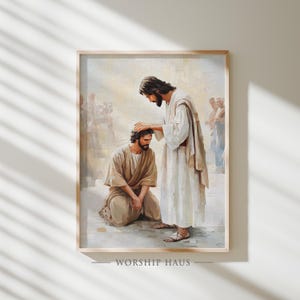 May include: Framed religious artwork depicting a biblical scene. A man in a white robe places his hand on the head of a kneeling man in a tan robe. The artwork is in a wooden frame and features the text "WORSHIP HAUS" at the bottom.