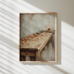 May include: A framed print of a vintage workshop scene. A wooden workbench is covered in wood shavings and tools, with a lit candle at the end. The artwork has a warm, neutral color palette and a rustic aesthetic. The text "WORSHIP HAUS" is at the bottom.