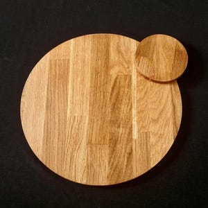 May include: A wooden serving board, circular in shape, with a smaller, attached circular piece. The board is made of light-coloured wood with visible grain patterns. The design is simple and natural, suitable for serving food or as a decorative item.