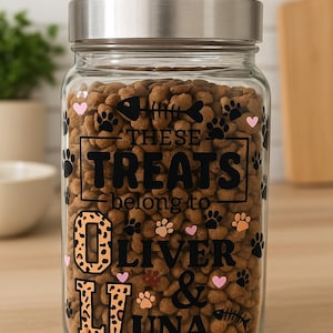 May include: A clear glass jar filled with pet food, topped with a silver lid. The jar is decorated with black paw prints, pink hearts, and the words "THESE TREATS belong to OLIVER & LUNA" in a mix of fonts.