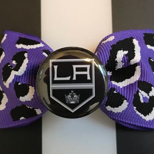 May include: Purple and black leopard print bow with a black and white LA Kings hockey team button.