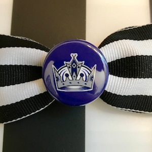 May include: A black and white striped bow with a blue button featuring a silver crown with a blue and white design.