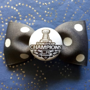 May include: Black and white polka dot bow with a 2012 Stanley Cup Champions button featuring the LA Kings logo.