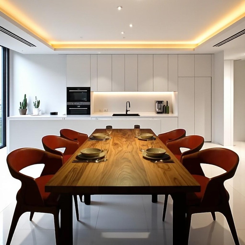 May include: A modern dining room with a long, wooden table set for a meal. Six red leather chairs surround the table. The room features white cabinets, a black oven, and a large window. The ceiling has recessed lighting.