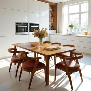 May include: A wooden dining table with six matching chairs. The chairs have reddish-brown leather seats and curved wooden backs. A vase of flowers sits on the table, along with a book. The kitchen has white cabinets and stainless steel appliances.