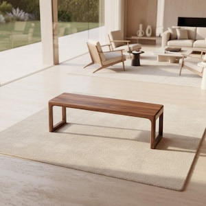 May include: A rectangular wooden bench with a rich brown finish. The bench has a minimalist design with a flat top and four legs. It is placed on a light beige rug in a modern living room setting. The bench measures approximately 60 inches in length.