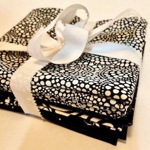 May include: A stack of black and white patterned fabric squares tied with a white ribbon. The fabric features a repeating pattern of white dots on a black background. The ribbon is tied in a bow.