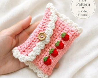 Könnte beinhalten: Ein kleines gehäkeltes Täschchen in Rosa mit weißem Wellenrand, einem Holzknopfverschluss und vier kleinen roten Erdbeerapplikationen mit grünen Blättern. Das Bild enthält den Text PDF Pattern + Video Tutorial.