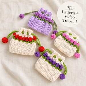 Puede incluir: Tres pequeñas bolsas de ganchillo con cordón y diseño floral. Una bolsa es de color lavanda sólido, mientras que dos son de color crema con filas de capullos rojos o morados. Cada bolsa tiene tallos y hojas verdes y cordones con pompones.