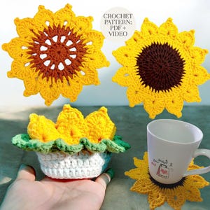 May include: Handmade crochet sunflower coasters and a small flower pot. The coasters are yellow with brown centers, resembling sunflowers. The flower pot is white with a green and white trim, holding yellow crochet flowers. The image includes the text "CROCHET PATTERN: PDF + VIDEO".
