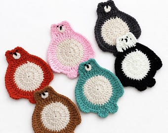 May include: A collection of six crocheted bear-shaped coasters in red, pink, brown, teal, black, and white, each featuring a circular cream-colored center and a small bear head. The text PDF Pattern + Video Tutorial is visible at the top.