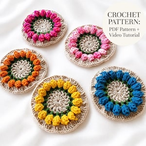 Könnte beinhalten: Fünf kreisförmige Häkeluntersetzer mit beiger Basis, einem Ring aus grünen Stielen und bunten Blütenknospen in Pink, Hellrosa, Orange, Gelb und Blau. Der Text oben rechts lautet: CROCHET PATTERN: PDF Pattern + Video Tutorial.