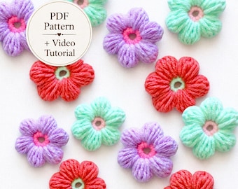May include: A collection of small, handmade yarn flowers in shades of mint green, lavender, and coral red. Each flower features a contrasting center ring. A circular white label with the text PDF Pattern + Video Tutorial is overlaid.
