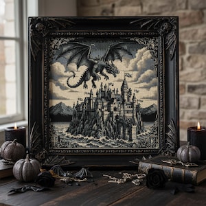 May include: A framed cross-stitch depicting a dragon soaring above a castle on a rocky island. The artwork is in shades of gray and black, with a detailed frame. The scene includes clouds, water, and flags. Decorative pumpkins and candles surround the frame.